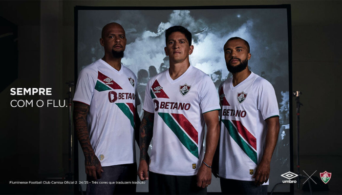 Camisa reserva do Fluminense para a temporada 2024-2025. A camisa branca apresenta duas faixas diagonais em verde e grená, com texturas que lembram a areia da praia e monogramas do clube. Gola V branca, mangas brancas com punhos nas cores do clube, escudo do Fluminense bordado no lado esquerdo do peito, logo da Umbro bordado no lado direito do peito